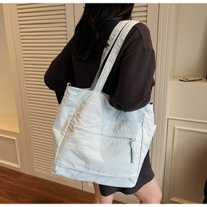 Large light blue tote bag shown on shoulder with focus on front zipper and textured fabric