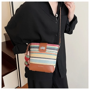 Detail of striped straw bucket bag with strawberry charm and metal chain strap
