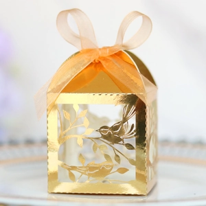 Macro shot of golden laser-cut favor box with bird pattern and organza ribbon bow