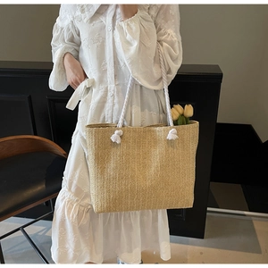 Detail of hand-woven straw tote bag with thick white cotton rope handles and floral accent