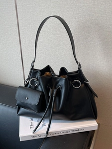 Minimalist black leather tote bag with silver rings and drawstring closure on a sofa