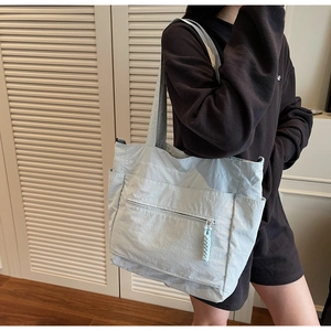 Light blue nylon tote bag with side pockets and front zipper on a model for daily use