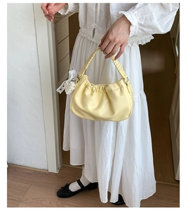 Detail of light yellow ruched cloud bag with woven handle and lace heart charm
