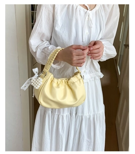 Close-up of pleated cream dumpling bag with woven handle and pearl heart charm accessory