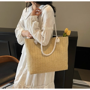 Detailed view of straw woven tote bag with white cotton rope handles and floral accent