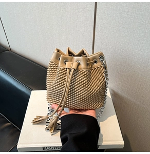 Detail of woven bucket bag with drawstring tassel closure and silver chain strap