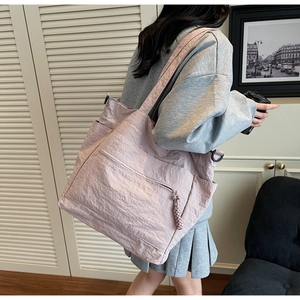 Detail of a pink tote bag with pleated nylon texture and wide strap worn by a model