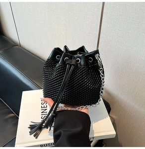 Detail of black bucket bag with woven texture, drawstring closure and silver chain strap