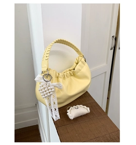 Detail of yellow pleated cloud bag featuring woven handle and pearl heart pendant charm