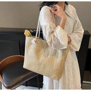 Detail of a large straw tote bag with white rope handles and vertical woven textures