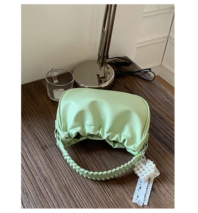 Detail of light green pleated handbag featuring a woven handle and pearl heart charm