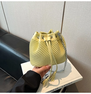 Close-up of a pale yellow bucket bag with woven texture, silver chain and tassels