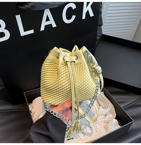Detail of light yellow woven bucket bag with drawstring closure and silver chain strap