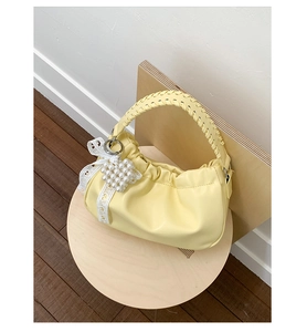 Detail of light yellow ruched cloud bag featuring a woven handle and pearl bow charm
