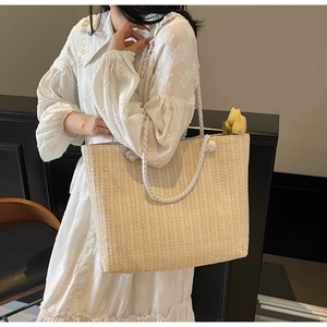 Detail of beige straw tote bag featuring wavy texture and thick white cotton rope straps