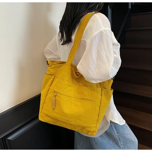 Detail of a bright yellow nylon tote bag showing the side pocket and woven zipper pull