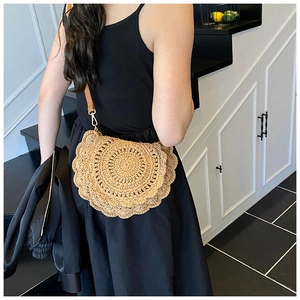 Detail of hand-woven straw saddle bag with wavy scalloped edges and leather strap