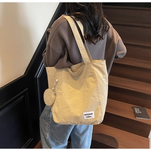 Close-up of beige canvas tote bag with a small round coin purse charm on a wooden staircase