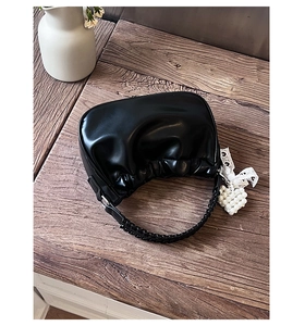 Detail of black pleated cloud bag with woven handle and pearl heart charm accessory