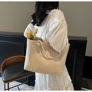 Detail of beige straw woven tote bag featuring white rope handles and chic knotted accents