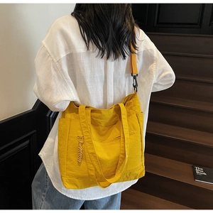Detailed view of yellow tote bag featuring dual straps and side pocket on a model