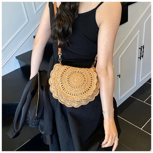 Detail of woven straw saddle bag with intricate petal patterns and thin leather strap