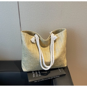 Detail of straw woven tote with thick cotton rope handles and tassel accent on a book