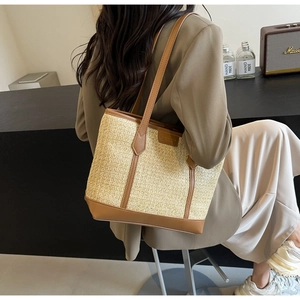 Straw tote bag with brown leather handles worn over the shoulder for daily commute