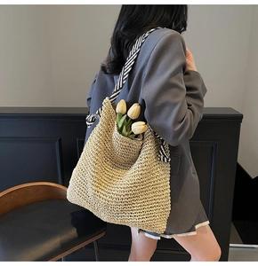 Detail of woven straw tote bag with black and white striped strap on shoulder