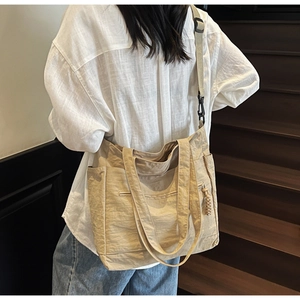 Side view of a large beige nylon tote bag with adjustable strap worn by a model