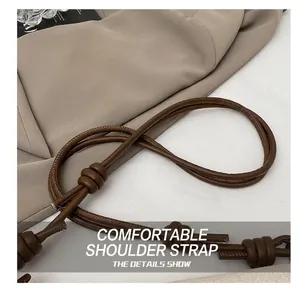 Détail de la bandoulière en cuir marron noué avec une texture fine sur un tissu kaki