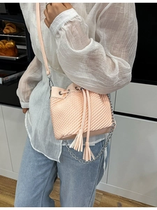 Pink woven bucket bag with fringe tassels and leather chain strap shown on a model