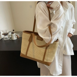 Woven straw tote bag with brown leather straps shown on shoulder for daily commute