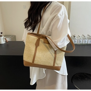 Detail of woven straw tote bag with brown leather trim and dual handles in a cafe setting