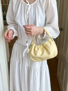 Pale yellow pleated cloud bag with woven handle and lace pearl bow on a female model