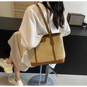 Detailed view of woven straw tote bag with brown leather straps held by a model