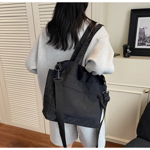 Close-up of black nylon tote bag showing front zipper pocket and adjustable strap