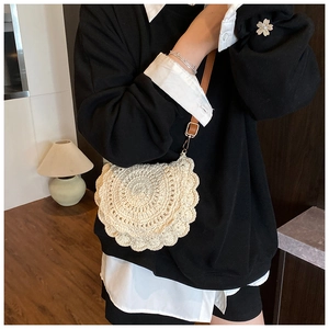 Detail of hand-woven cream crochet saddle bag featuring brown leather strap and gold buckle