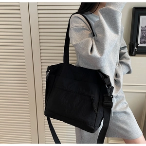 Detailed view of a black nylon tote bag on a model featuring a front zipper pocket