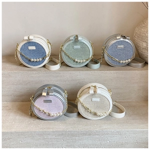 Group of small round woven crossbody bags in pastel colors with pearl chain details