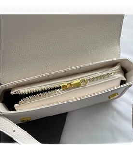 Close-up of smooth gold zipper and pebble leather texture on a white shoulder bag