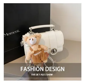 Close-up of white patent leather handbag featuring a silver lock and teddy bear charm