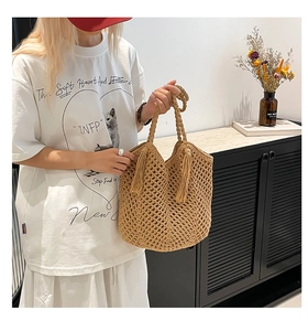 Detail of light brown hollow-out woven tote bag featuring tassel accents and a soft handle