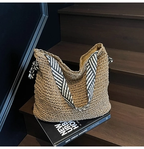 Detail of hand-woven straw tote bag with black and white striped wide shoulder strap