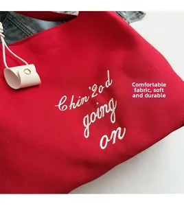Détail d'un cabas en toile rouge avec broderie blanche et breloque en cuir beige