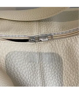 Detail of polished silver metal zipper on off-white lychee grain leather tote bag