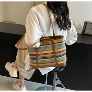 Detail of colorful woven tote bag with brown leather handles worn by a model