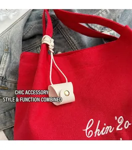 Détail du cabas en toile rouge avec broderie blanche et accessoire en cuir beige suspendu