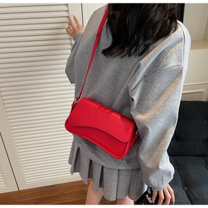 Detail of red pebbled leather crossbody bag with curved flap shown on model