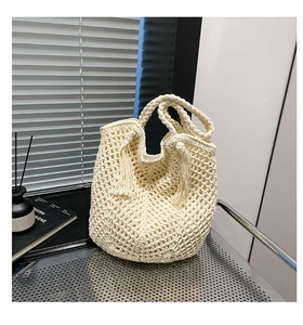 Detail of cream woven tote bag featuring decorative long tassels and hollow knit texture